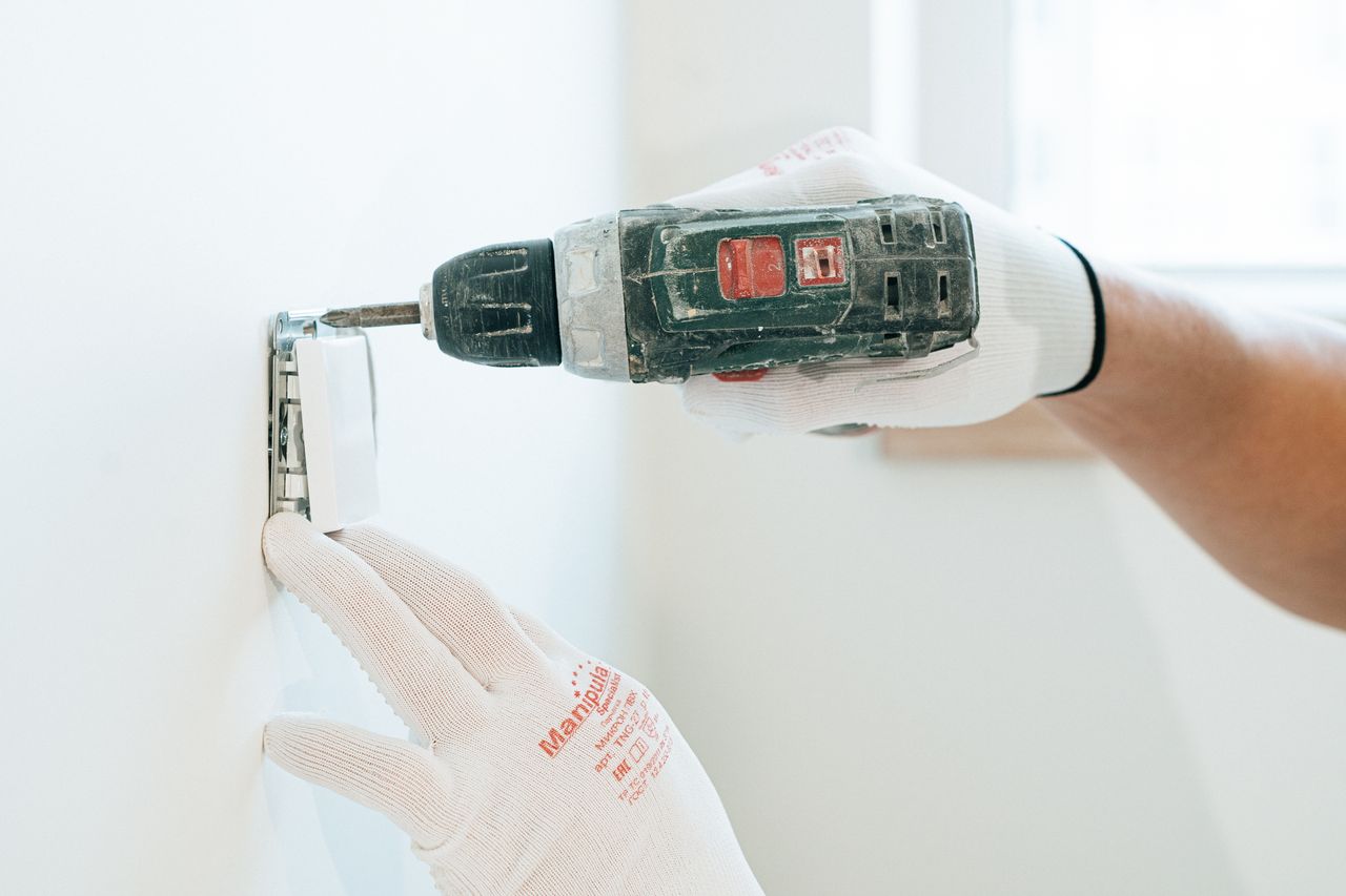 Crafting Captivating Headlines: Your awesome post title goes here Gloved hands using a drill to install a power outlet on a wall, focusing on precision and safety.