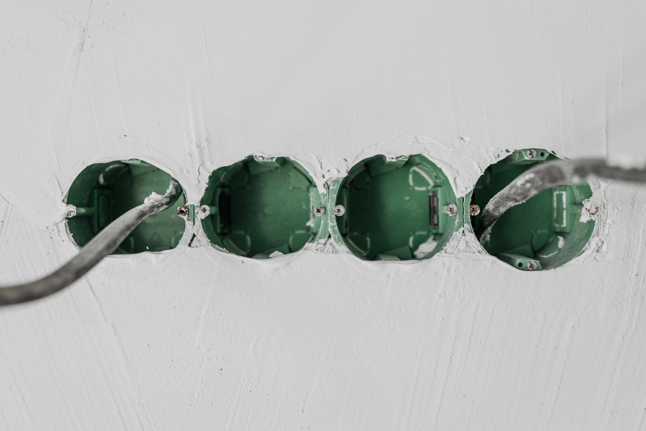our-value Close-up of green electrical boxes and wiring in a wall setup.
